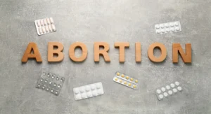 Wooden letters spell ABORTION on a gray surface, surrounded by blister packs of pills.