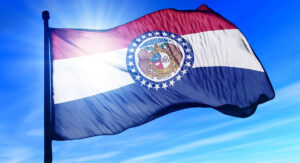 Missouri state flag waving in the wind with the state seal centered on a blue field of stars against red, white, and blue stripes.